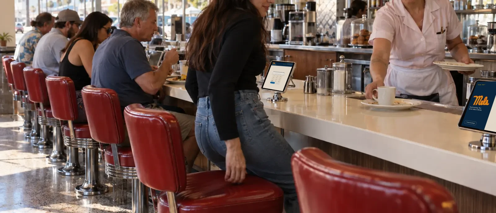 Concept render: a guest slides onto a red counter stool while a server sets down a plate, tablets on stands along the counter